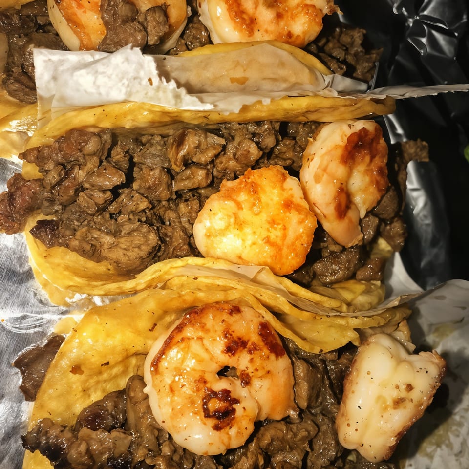Close-up of three The Taco Place tacos filled with beef and topped with grilled shrimp.