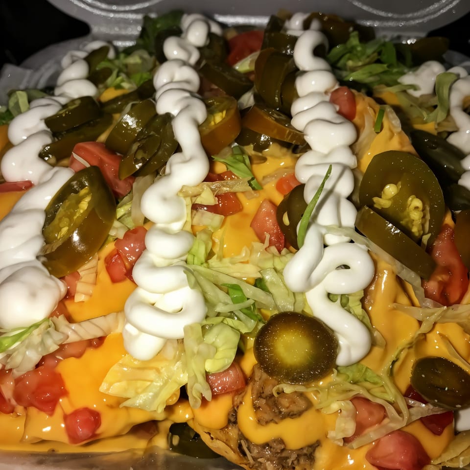 Close-up of The Taco Place's nachos with cheese, jalapeños, lettuce, tomatoes, and sour cream.