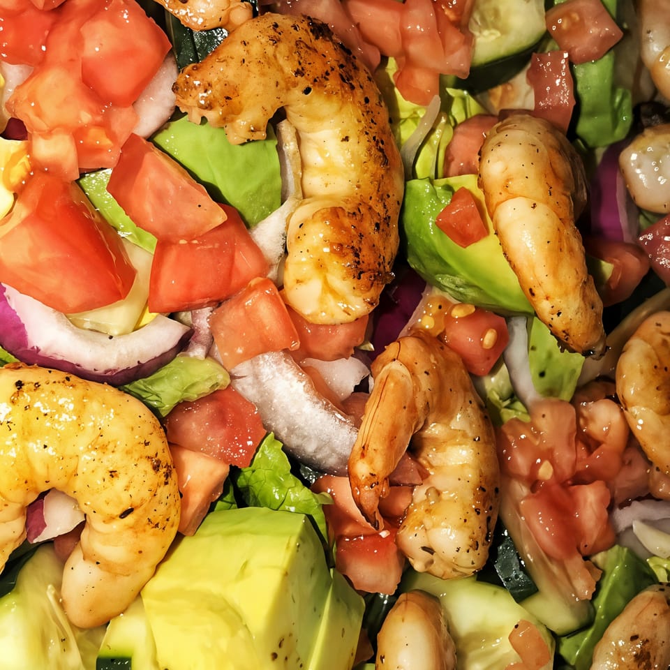 Close-up of a vibrant shrimp salad with diced tomatoes, avocado, red onion, and lettuce.