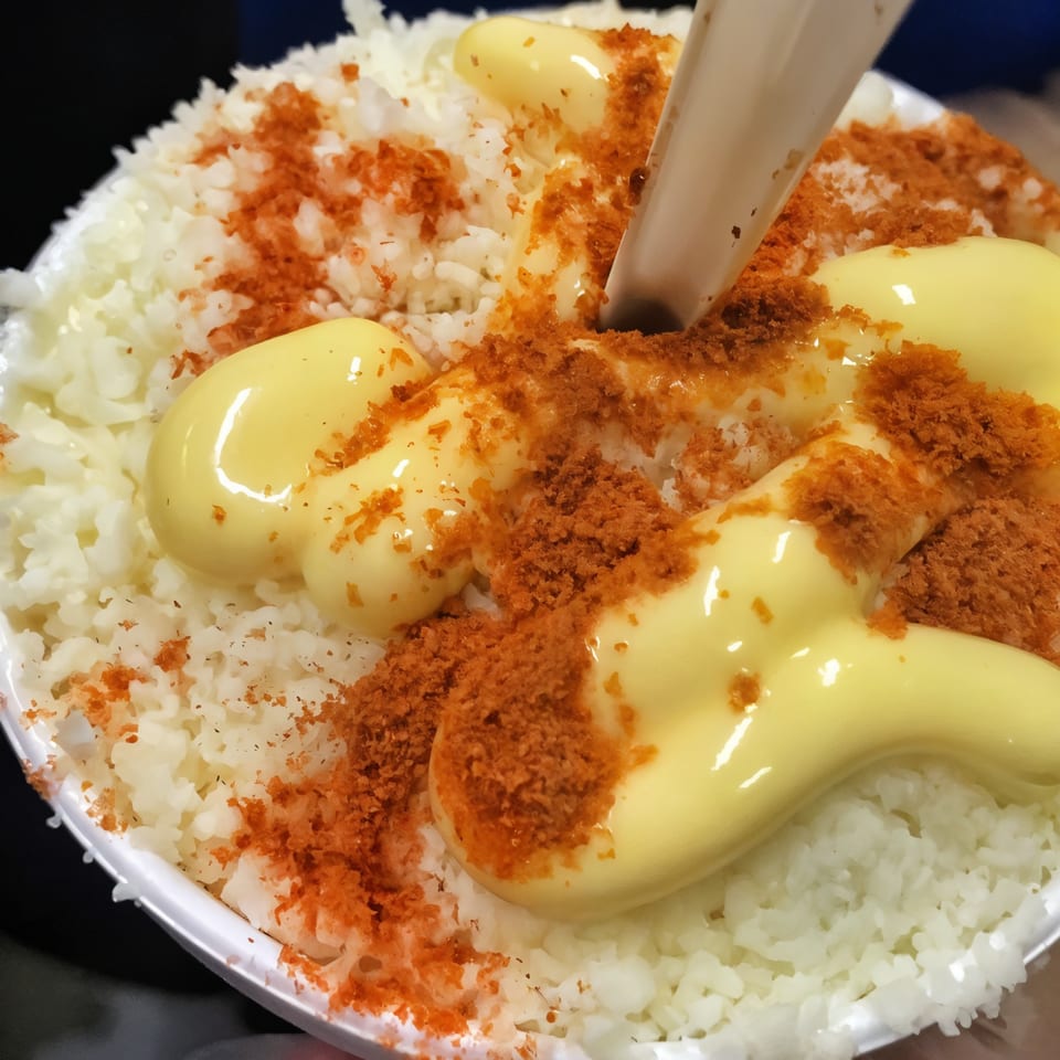 Mexican street corn in a cup with white corn, yellow sauce, and red seasoning.
